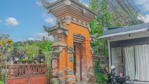 Une porte traditionnelle ornée de sculptures complexes, une moto garée à proximité et, au fond, un bâtiment dont le toit est fait de tôles ondulées.