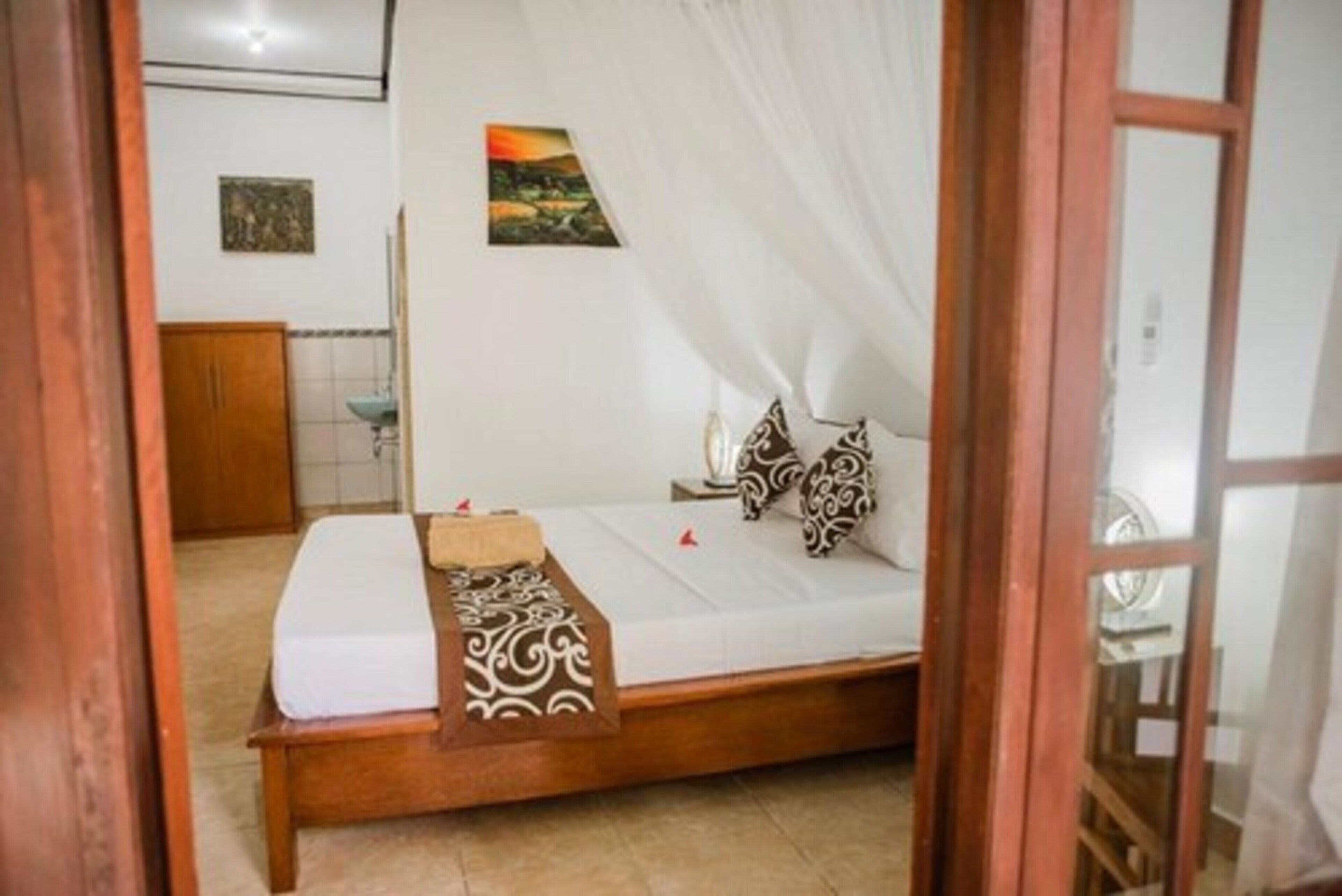 A bedroom with a wooden bed, white bedding, a patterned throw, and two pillows.