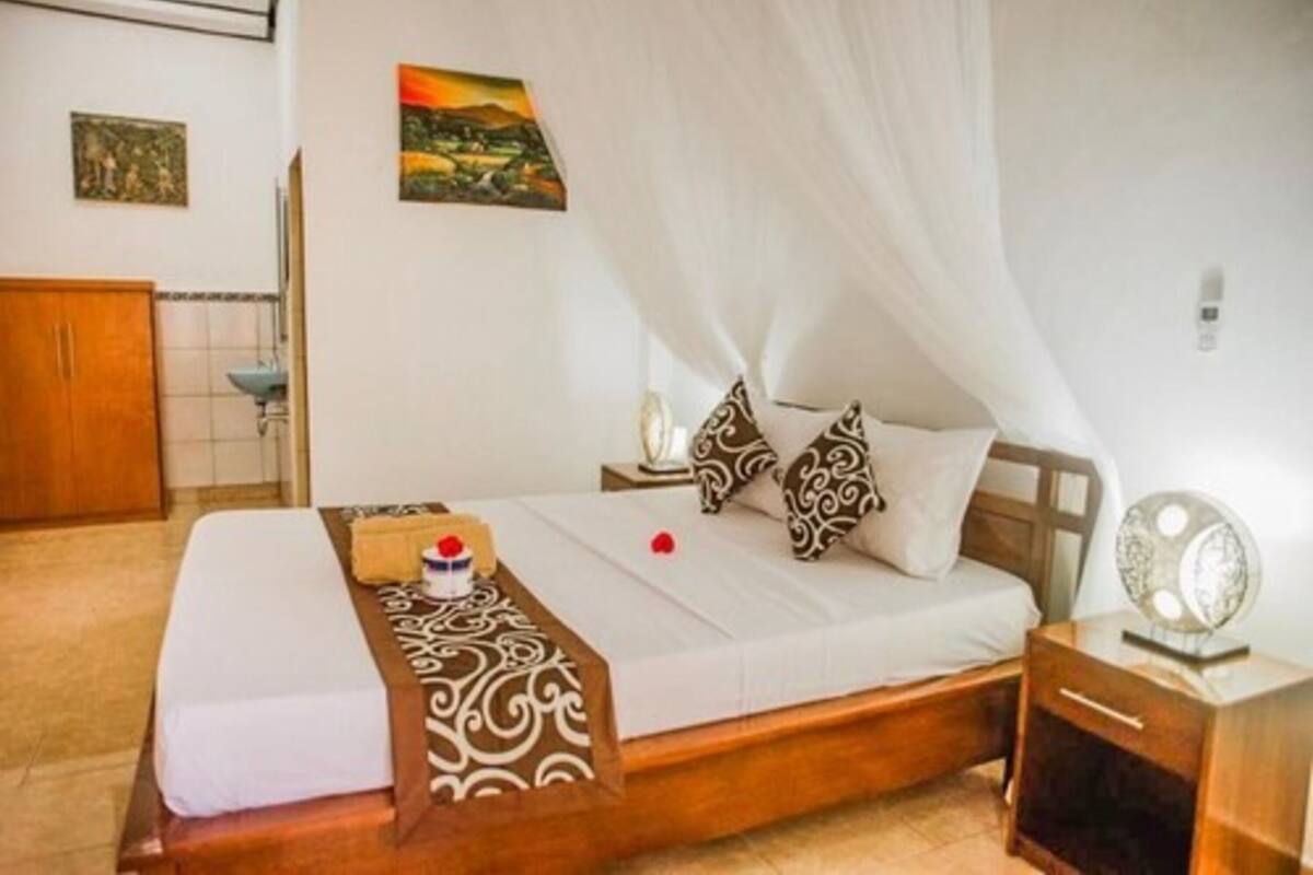 A neatly made bed with a canopy, a bedside table with a lamp, and a wall-mounted picture.