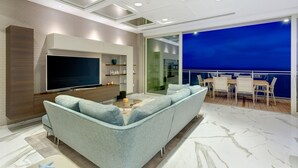 A modern living room with a large flat-screen TV, a light blue sofa, and a balcony with a view of the sea. - Super Luxury Apartment in Tigne Point, Amazing Ocean Views (Sliema)