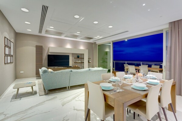 A modern living room with a sofa, TV, and dining area with a table set for four.