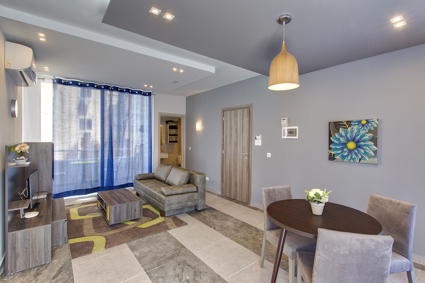 A modern living room with a sofa, a coffee table, a dining table with chairs, a TV, and a painting on the wall.