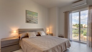 Une chambre à coucher avec un lit, des tables de chevet, un tableau et une vue sur l’extérieur, grâce à une grande fenêtre.