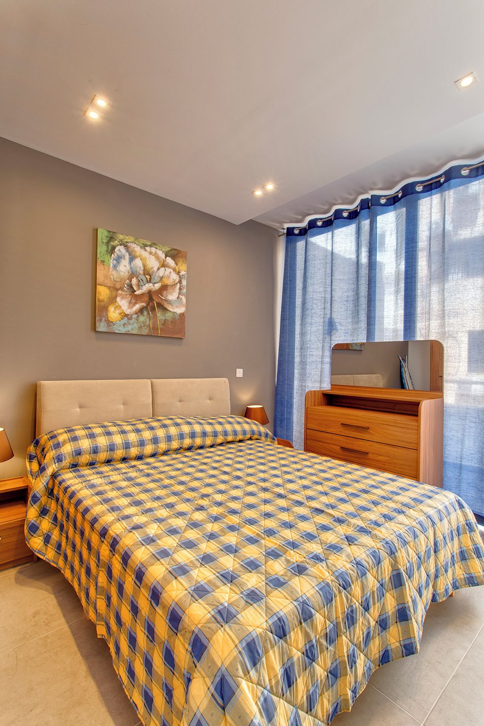 Une chambre à coucher avec un grand lit, une commode en bois, un tableau au mur et une fenêtre avec des rideaux.