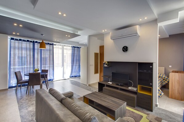 Ein modernes Wohnzimmer mit Sofa, Couchtisch, Fernseher und Essbereich mit Stühlen und Tisch.