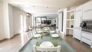 Un'ampia sala da pranzo con un lungo tavolo apparecchiato per un pasto, circondato da sedie bianche.