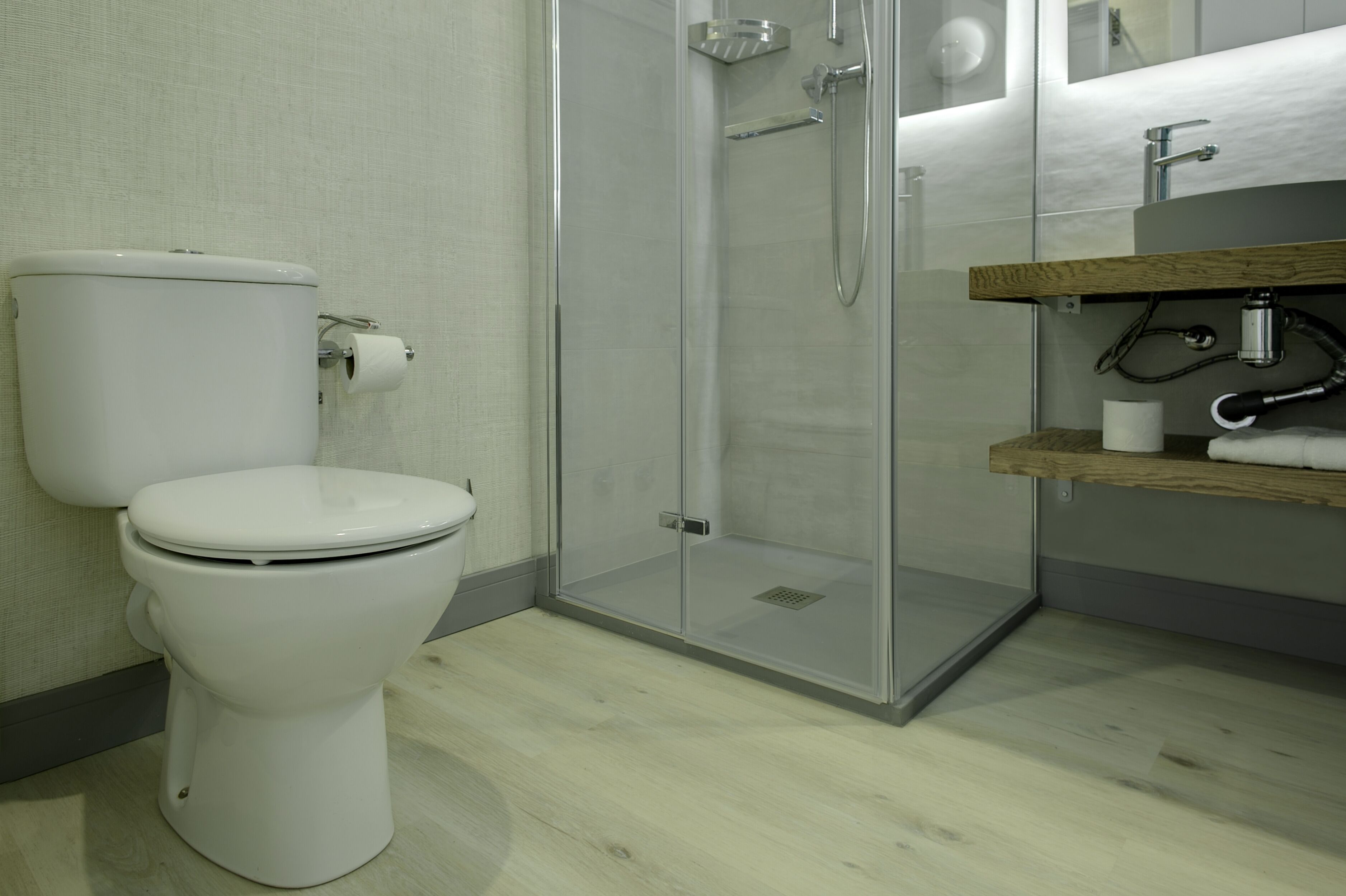 A modern bathroom with a toilet, a glass-enclosed shower, and a wooden vanity with a sink.