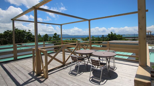 Una terraza de madera con una mesa y sillas, con vistas panorámicas a montañas y al mar.