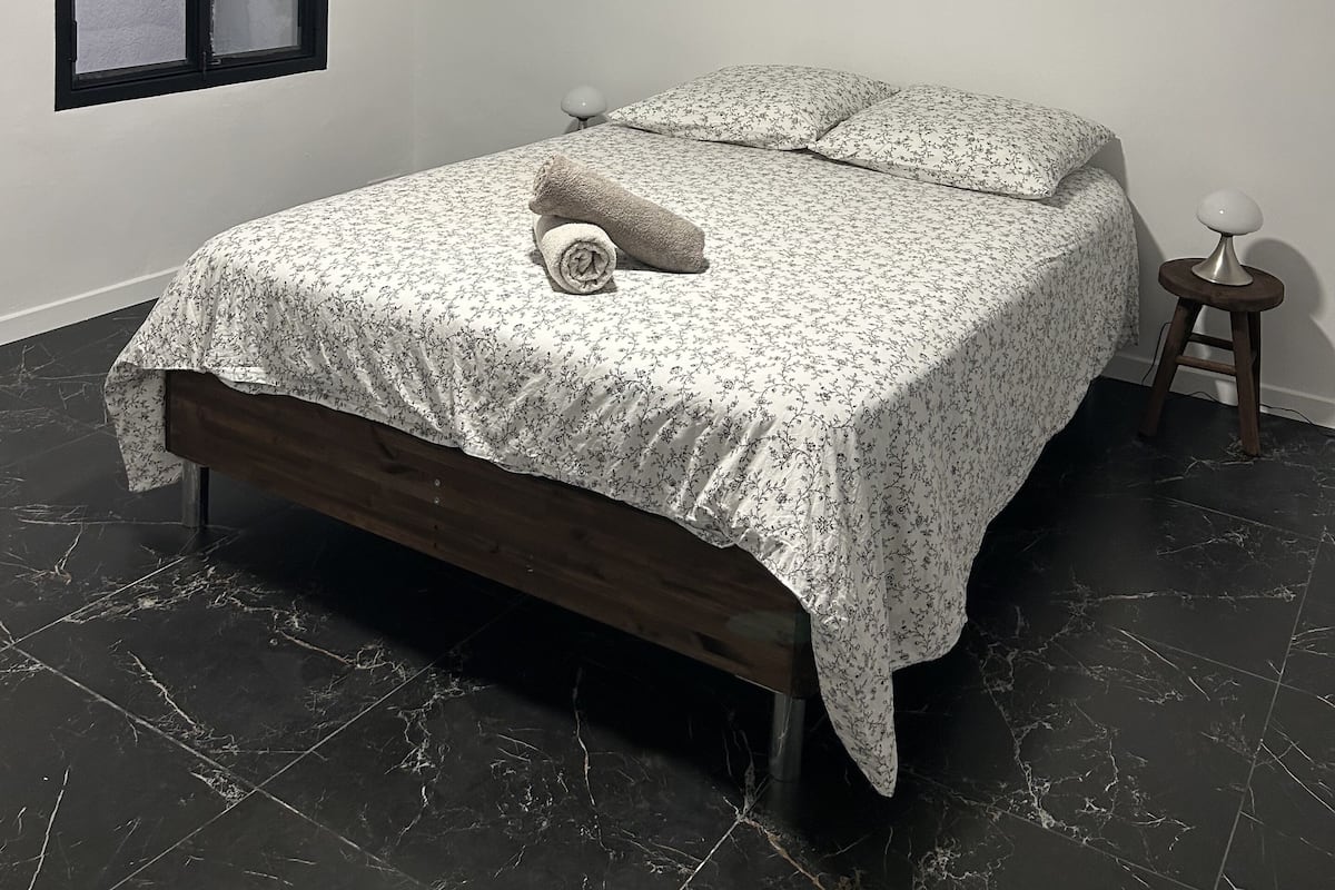Une chambre à coucher avec un lit, une fenêtre, une table de chevet et une lampe.