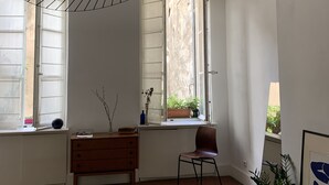 A bedroom with a bed, a chair, a dresser, a window with a view of greenery, and a unique ceiling light fixture. - Liberté (Marseille)