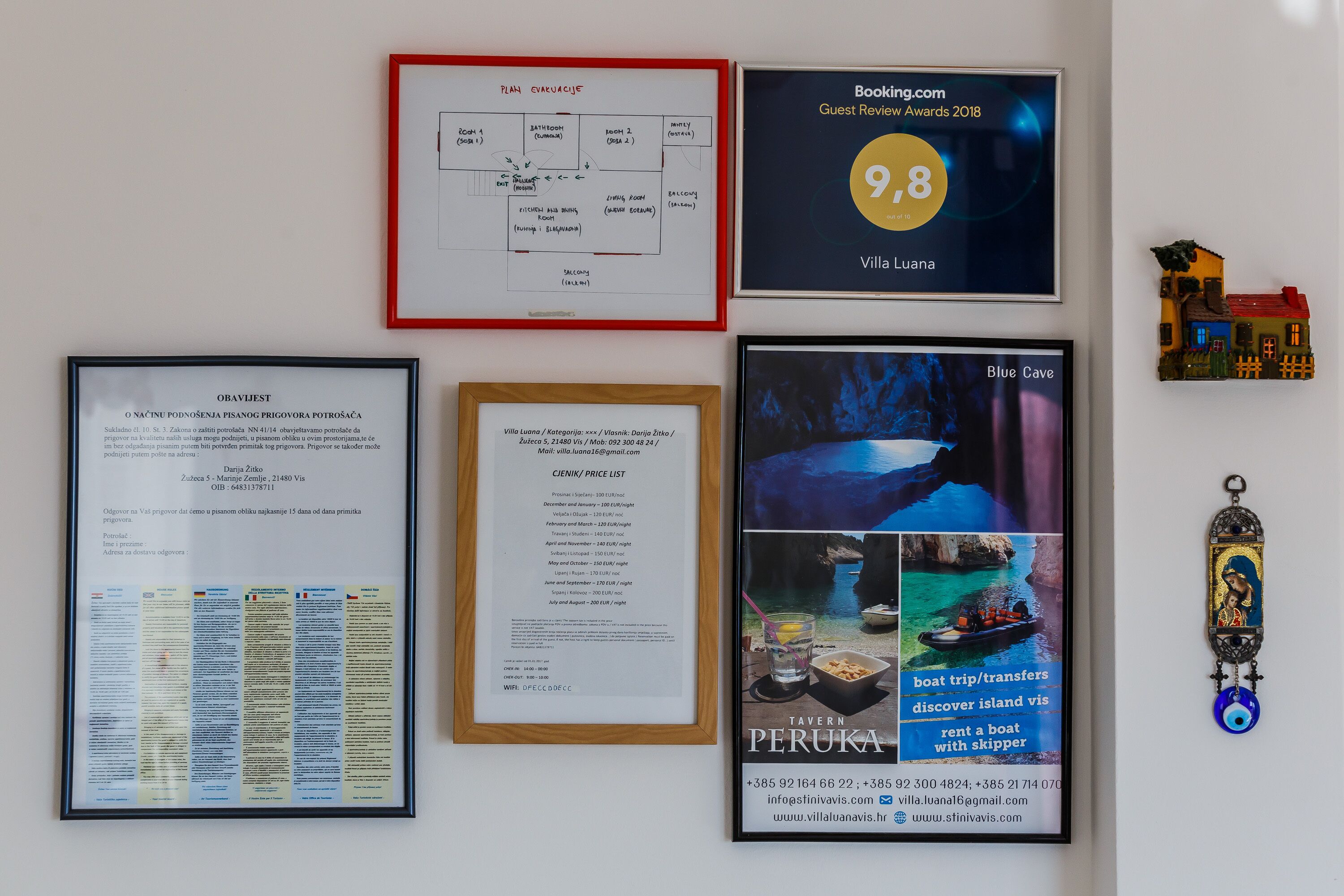 Una pared con varios documentos y premios enmarcados, incluyendo un premio por reseña de Booking.com, un diagrama de distribución de habitaciones y una lista de precios.