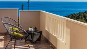A balcony with a wicker chair and table, overlooking a coastal view.