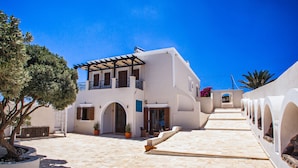 A white building with a balcony, a covered walkway, and a potted plant. - Grand Villa Santorini (Santorini)
