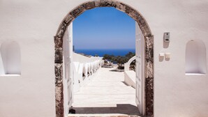 An arched doorway leading to a white-walled corridor with a view of the sea. - Grand Villa Santorini (Santorini)
