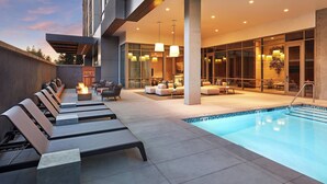 A modern outdoor pool area with lounge chairs and a fire feature, surrounded by glass walls and contemporary lighting. - AC Hotel by Marriott San Jose Santa Clara (Santa Clara)