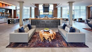 A spacious living area with a central coffee table, sofas, and a bar area with stools. - AC Hotel by Marriott San Jose Santa Clara (Santa Clara)