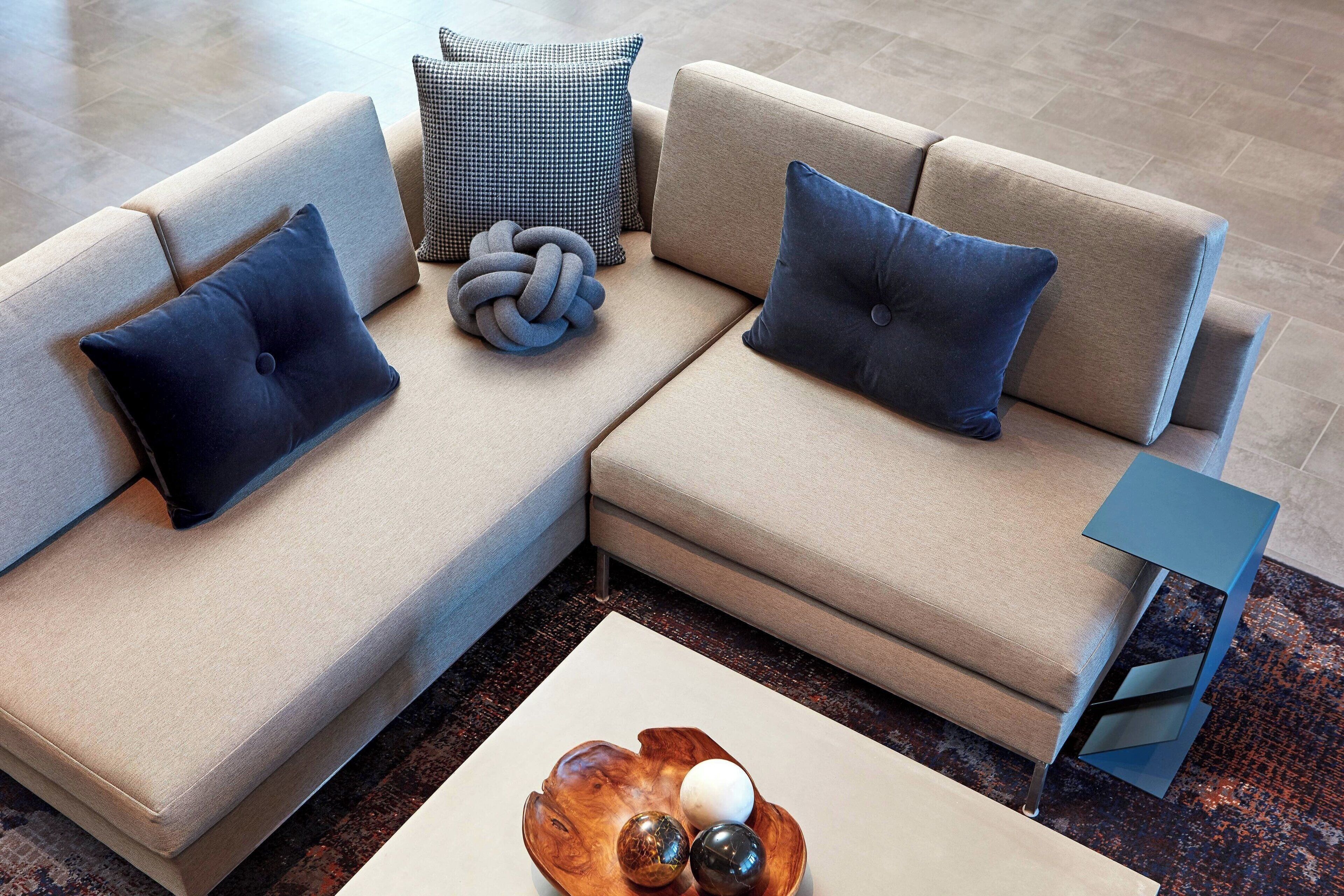 A modern living room with a beige sectional sofa, two dark blue pillows, a checkered throw pillow, and a wooden coffee table with decorative balls.