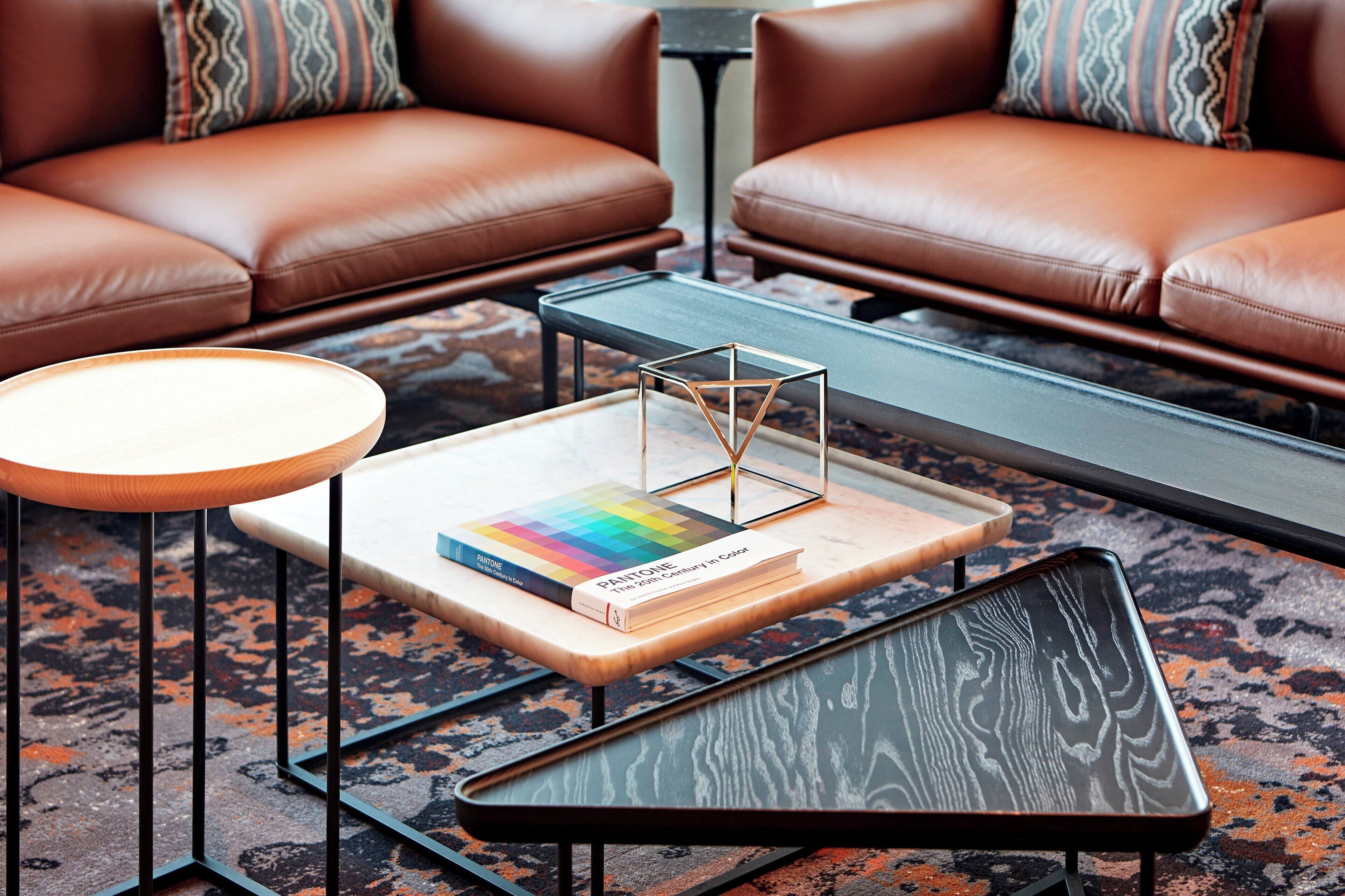A modern living room with leather sofas, a glass coffee table, and a book titled "Pantone Color."