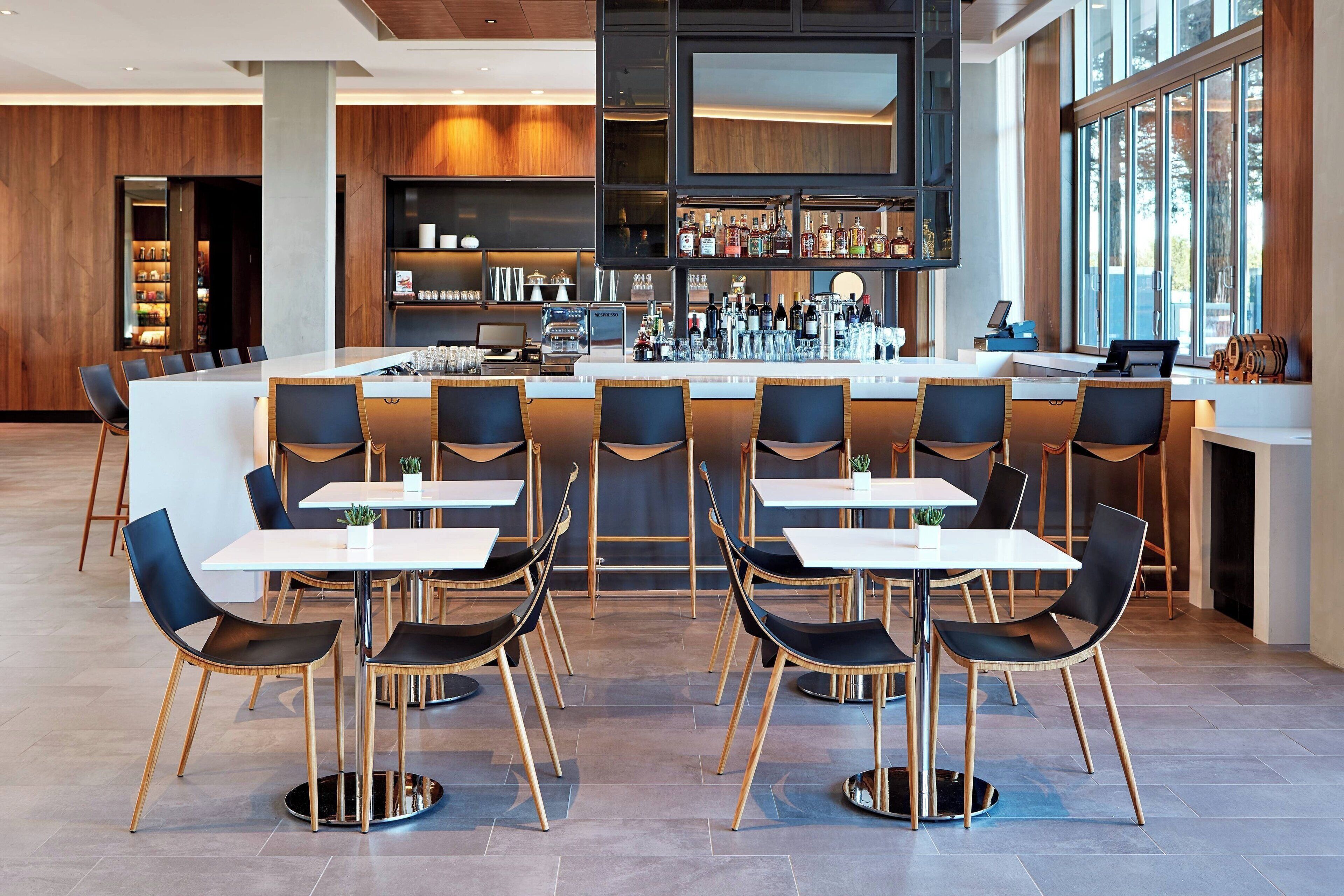 Uma área de bar moderna com um balcão comprido, várias mesas de apoio e banquetas.
