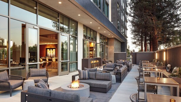 An outdoor seating area with sofas, tables, and a fire pit. - AC Hotel by Marriott San Jose Santa Clara (Santa Clara)