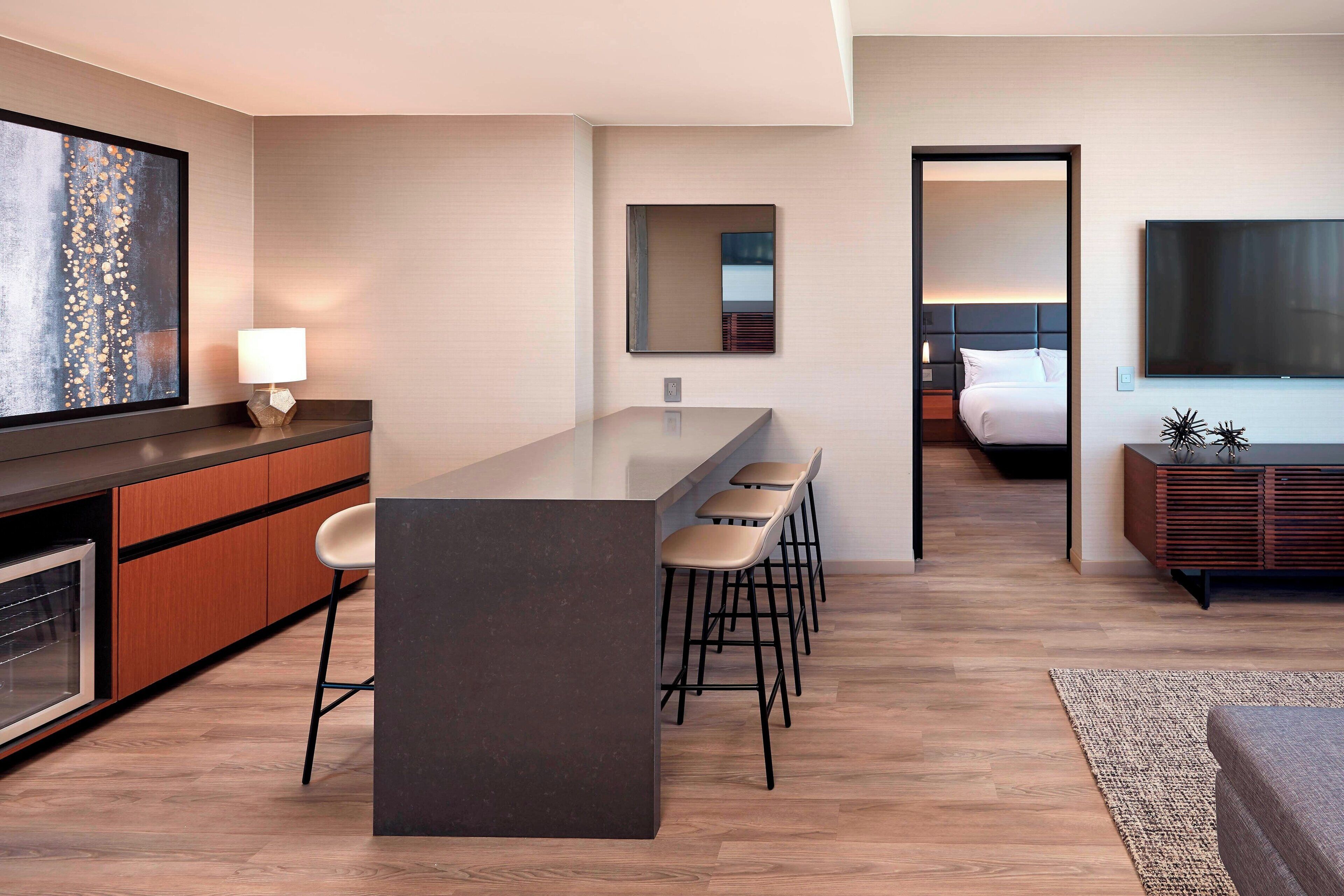 A modern hotel room with a kitchen area, a dining space, and a bedroom.