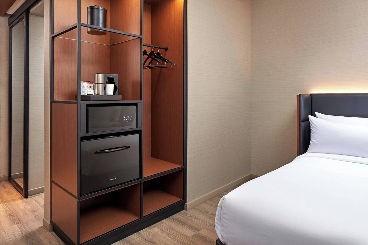 Ein Hotelzimmer mit einem Bett, einem Schrank mit Mikrowelle, einer Kaffeemaschine und einem Kleiderhaken.