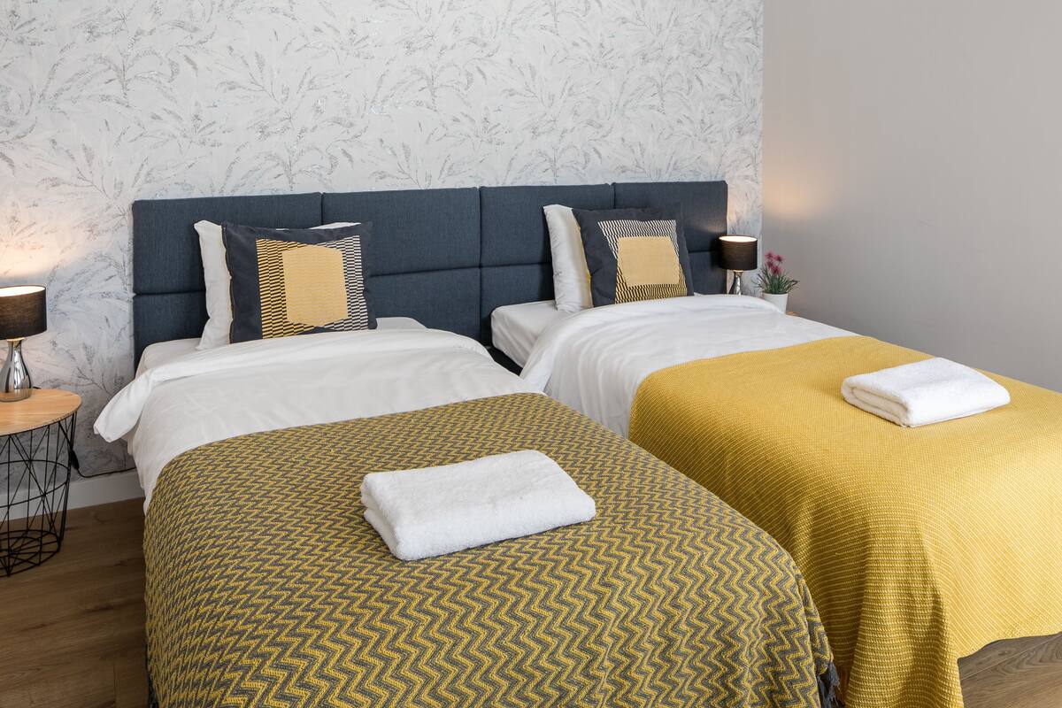 A hotel room with two beds, a round side table, a lamp, and a potted plant.