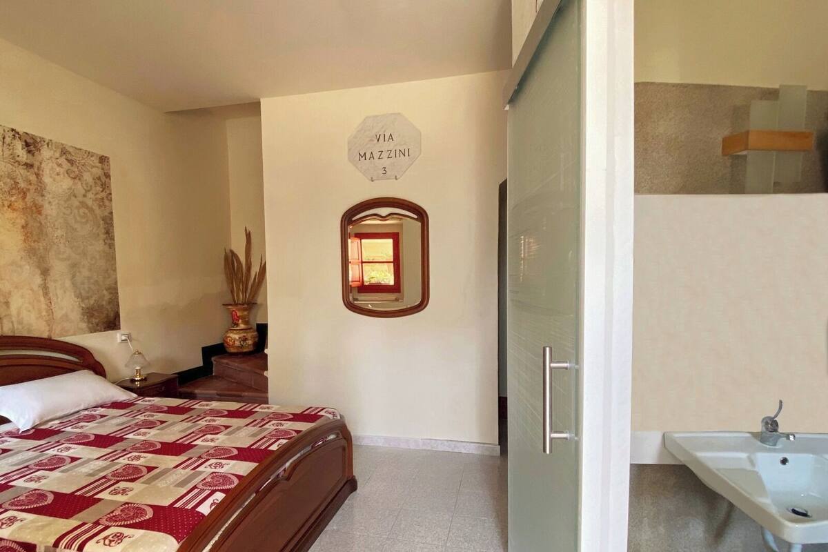 A bedroom with a bed, a bedside table, a mirror, a wall-mounted sign, and a bathroom with a sink.