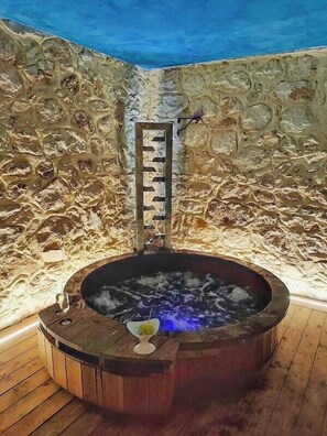 A stone-walled hot tub with a wooden bench and a metal ladder.