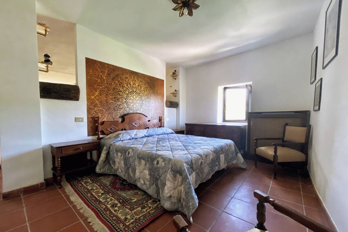 A bedroom with a bed, a chair, a patterned rug, and a decorative wall.