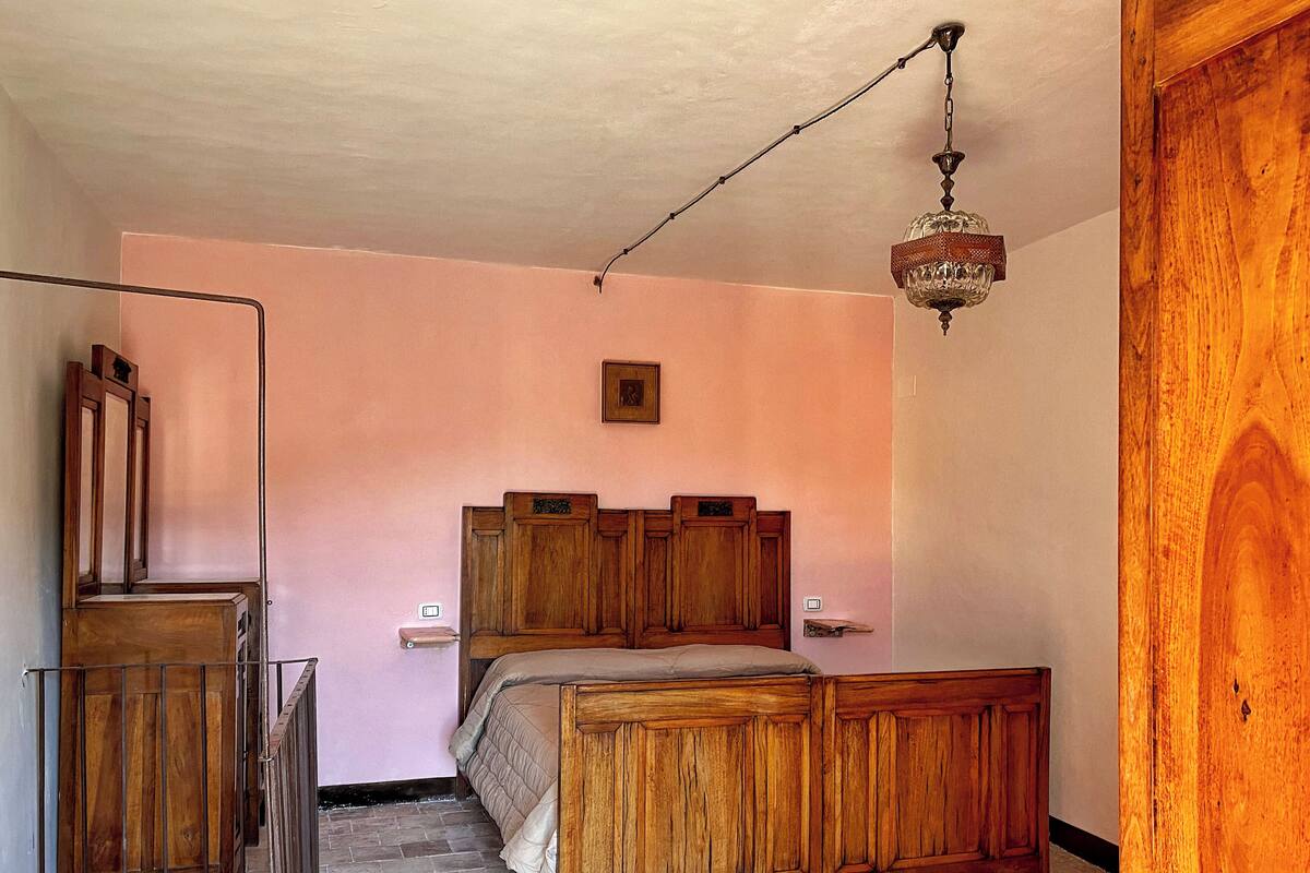 A bedroom with a wooden bed, a wooden wardrobe, a small bedside table, and a hanging light fixture.