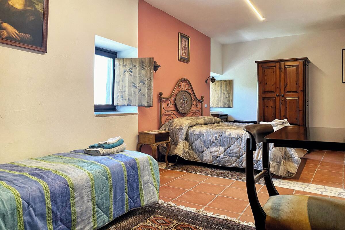 A bedroom with two beds, a wooden wardrobe, a window with curtains, and a painting on the wall.