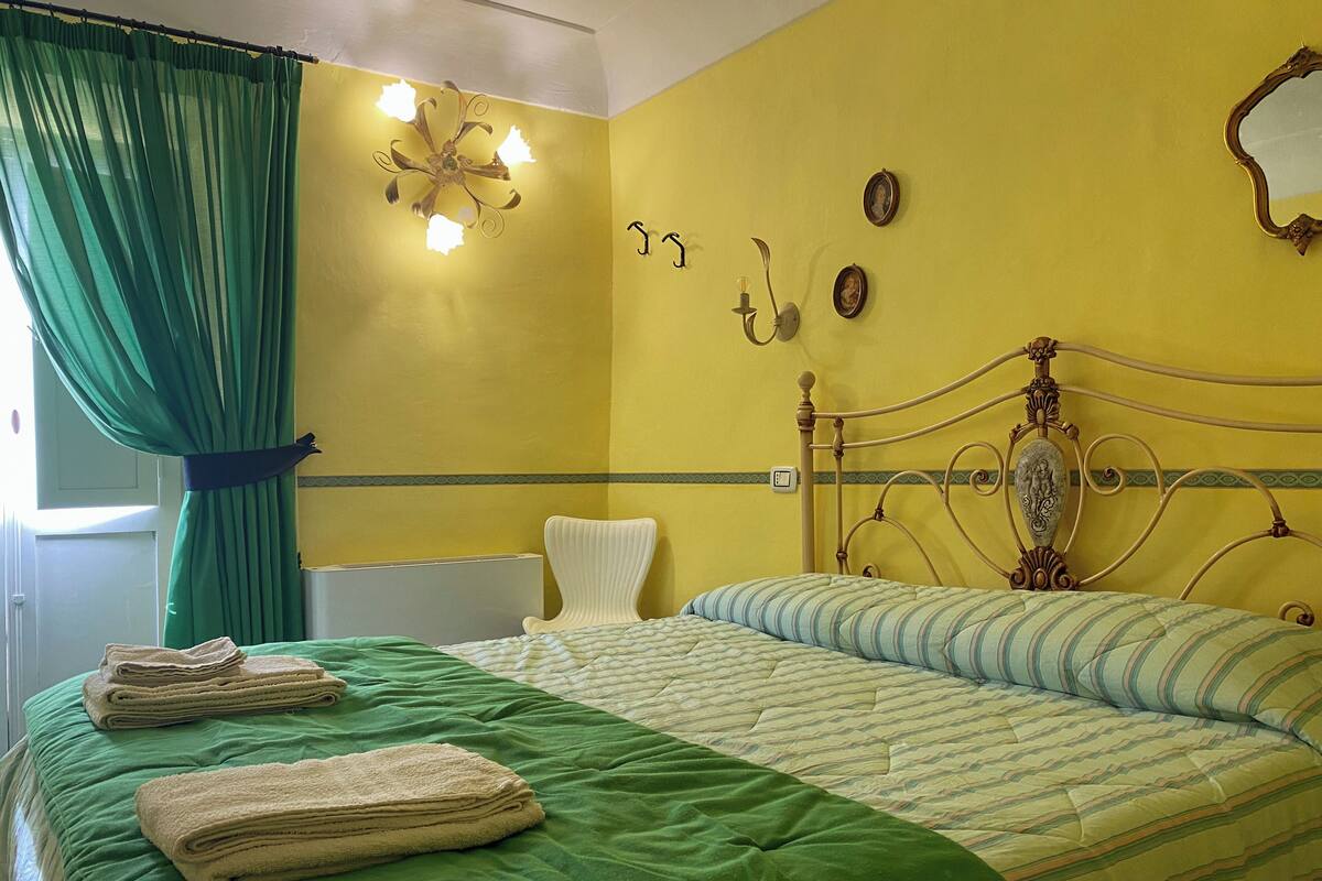 A room with a bed, green curtains, a wall clock, and a decorative mirror.