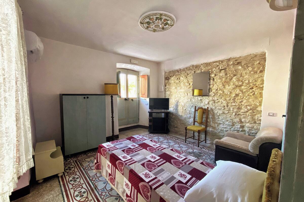 A bedroom with a bed, a desk, a chair, a television, and a stone wall.