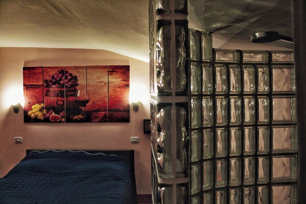 A bedroom with a bed, a wall-mounted painting, and a glass partition.