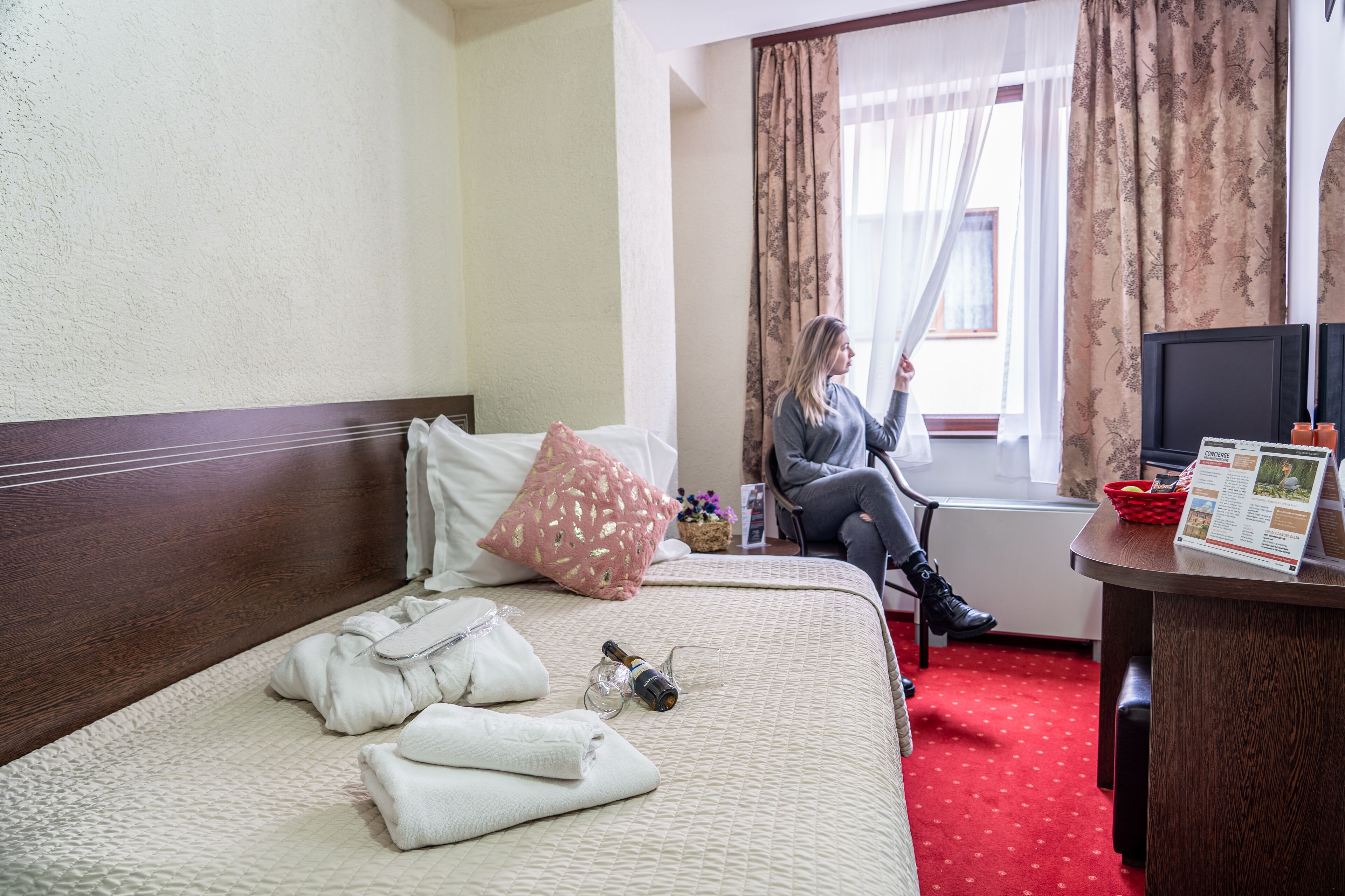 A hotel room with a bed, a desk with a computer, and a window with curtains.