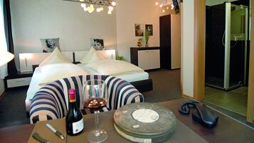 A hotel room with a bed, bedside table with a wine bottle and glass, a desk with a telephone, and a shower area.