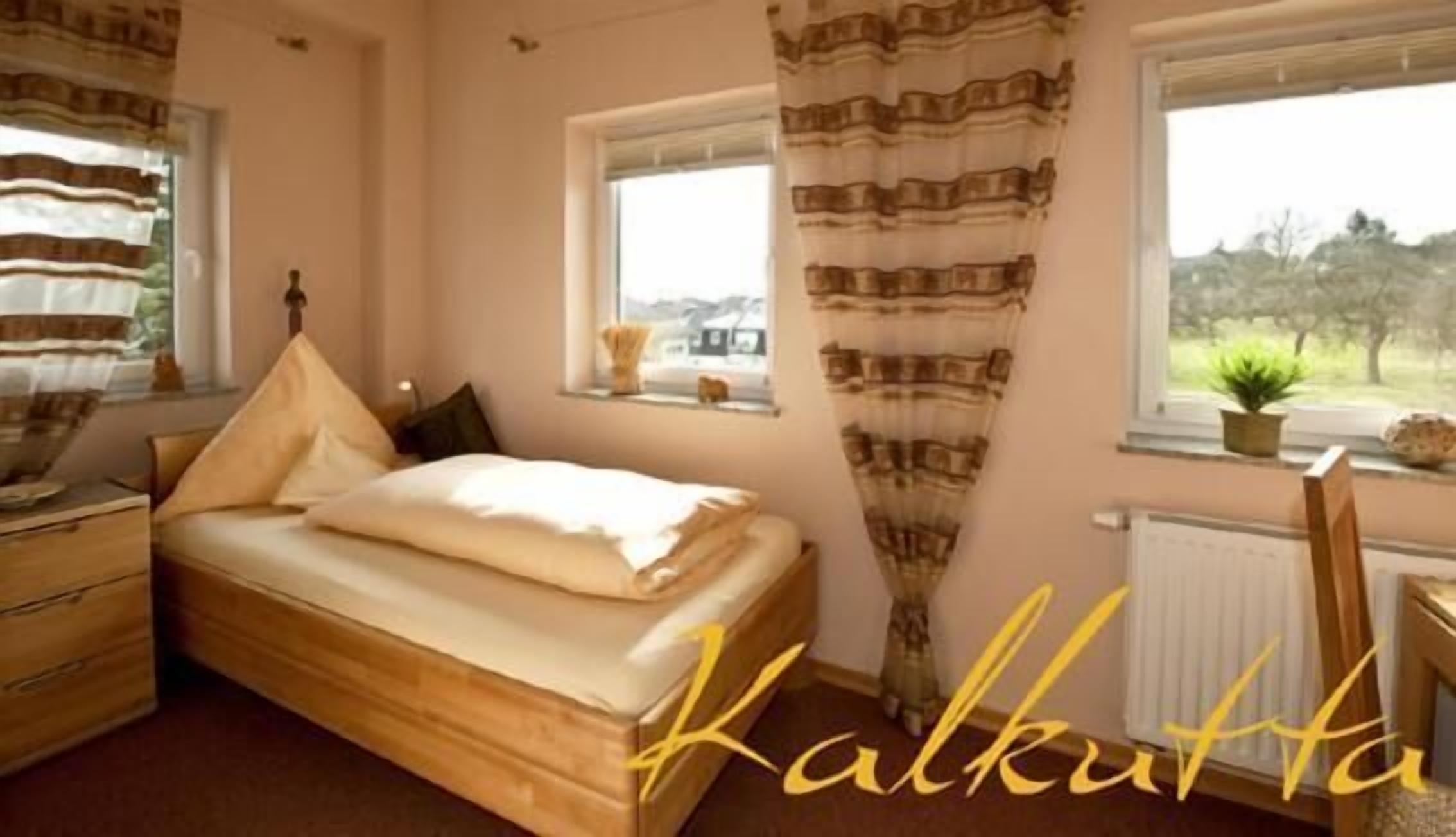 A bedroom with a wooden bed, a nightstand, a window with curtains, and a view of greenery outside.