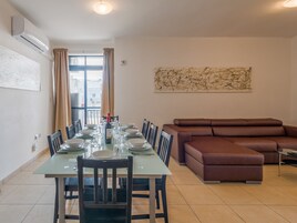 Un comedor con una larga mesa dispuesta para seis personas, rodeada de sillas, un sofá marrón y un cuadro abstracto grande en la pared.