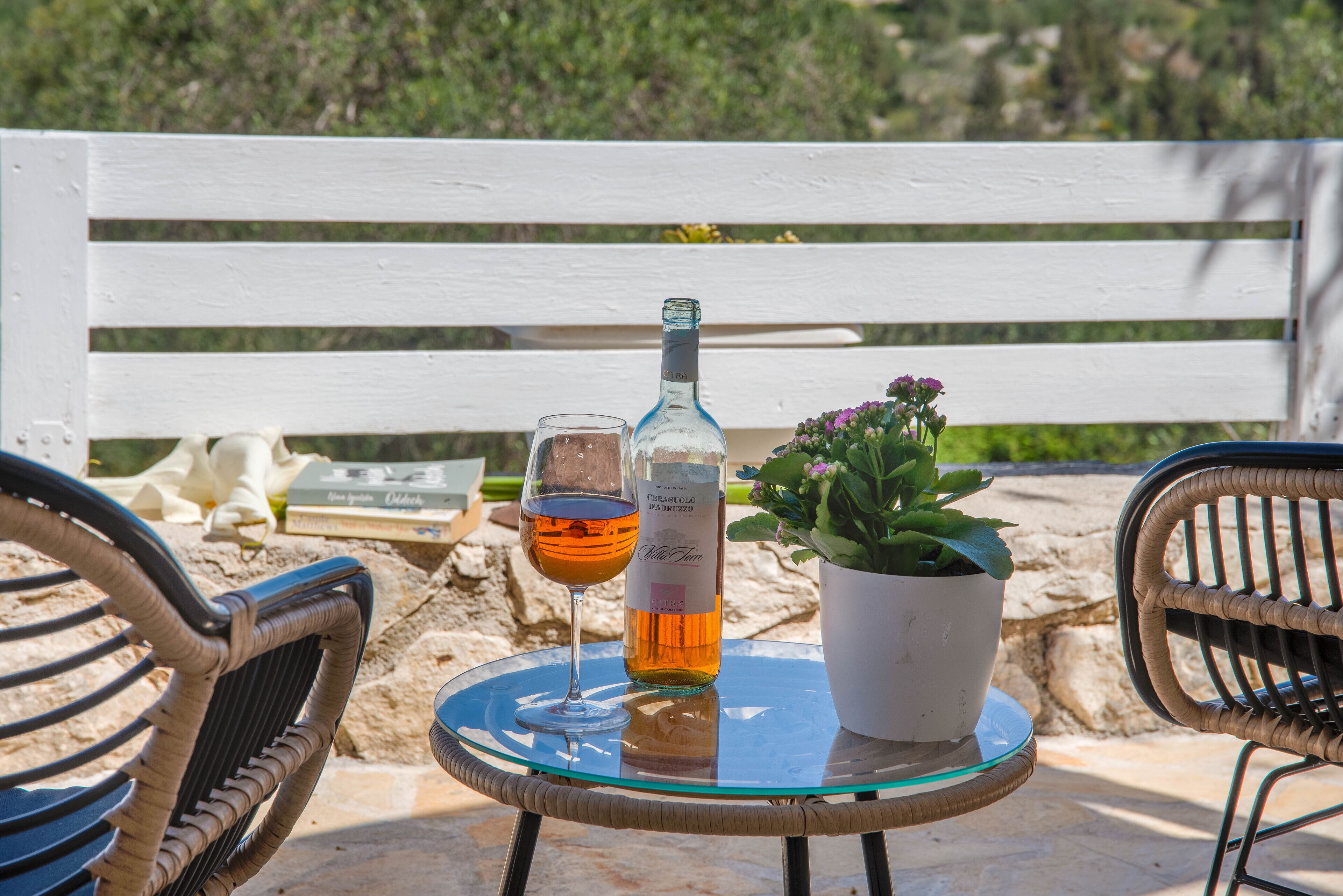 Een glazen tafel met een fles en een glas wijn, een potplant en een witte bank op de achtergrond.
