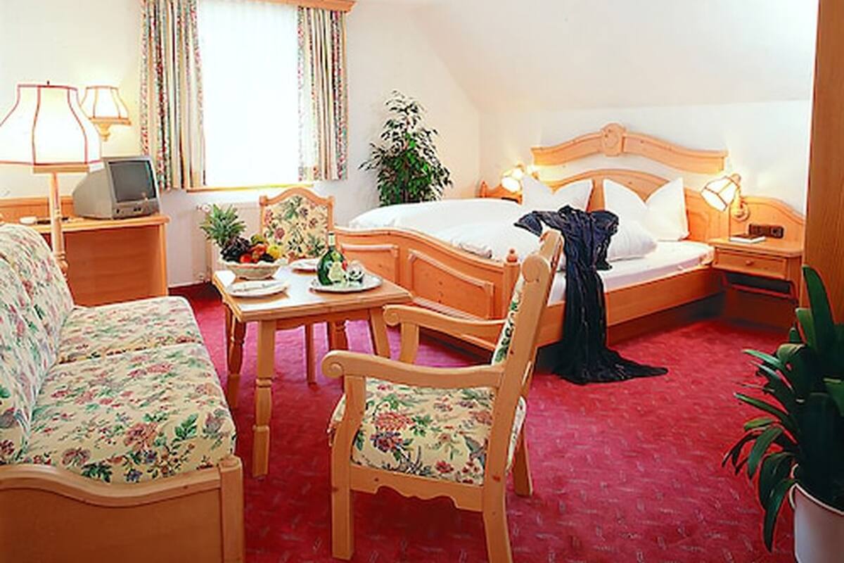 A hotel room with a bed, a desk, a chair, a sofa, and a potted plant.