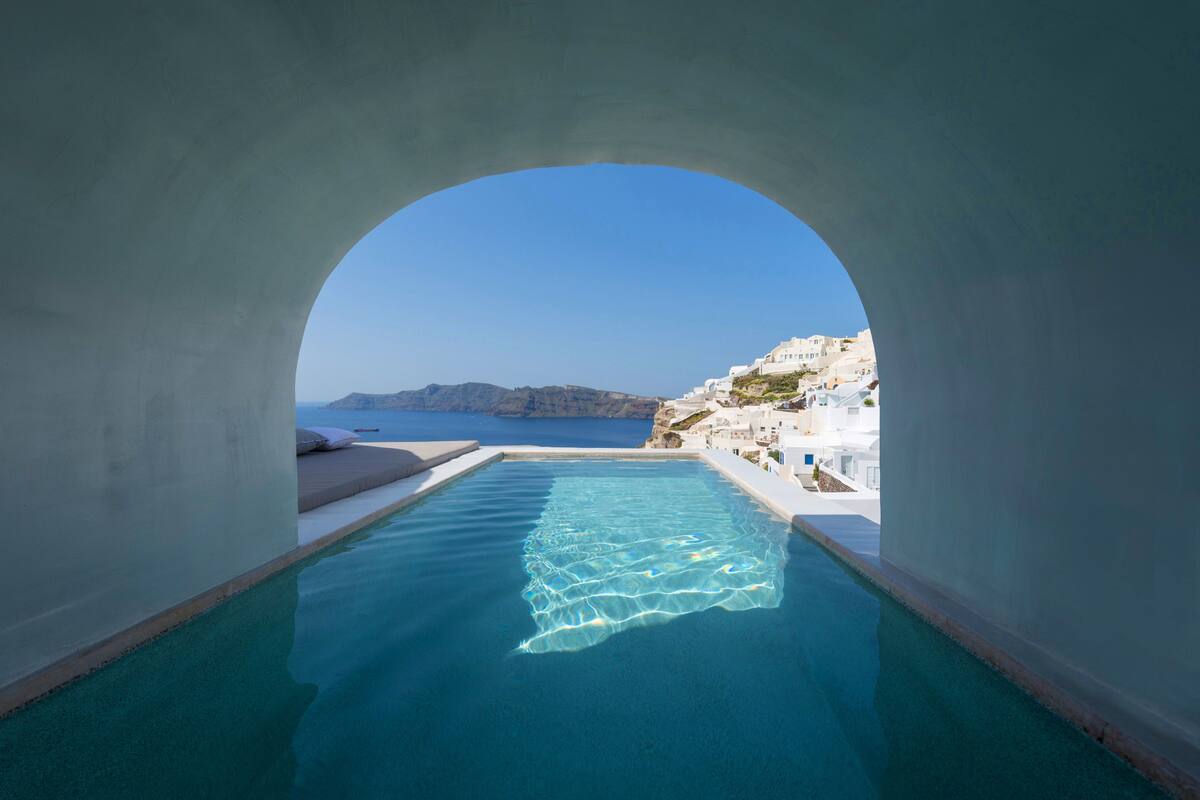 An infinity pool with a clear view of the sea and white buildings in the background.