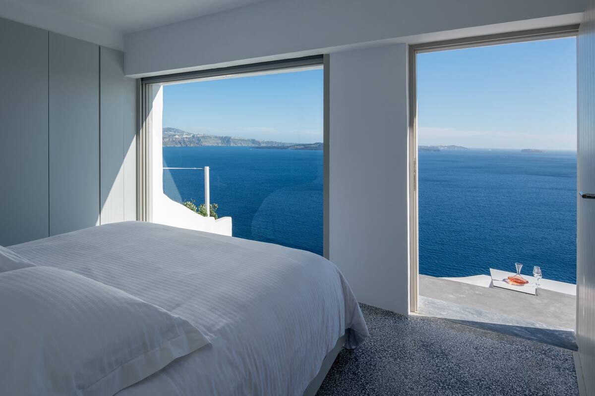 A bedroom with a large bed, a view of the sea, and a balcony with a table and chairs.