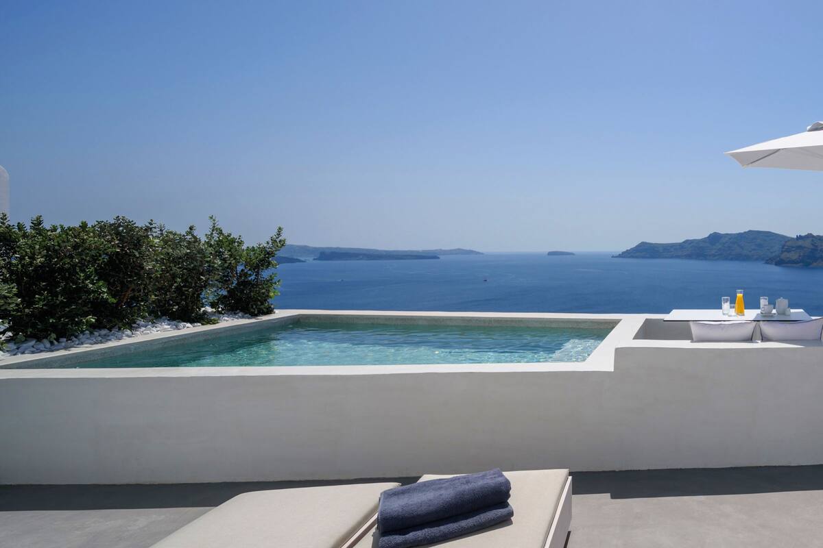 A rooftop infinity pool with a white umbrella, lounge chairs, and a view of the sea.