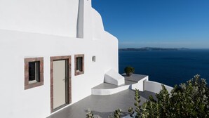 A white building with a door and windows, a small staircase, and a view of the sea. - Echoes Luxury Suites (Santorini)