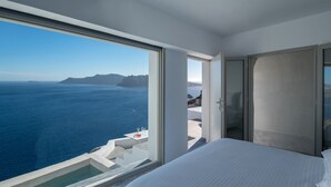 A bedroom with a large window overlooking a scenic ocean view. - Echoes Luxury Suites (Santorini)