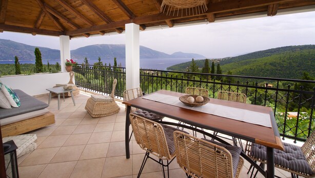 Un espacio de estar al aire libre cubierto, con una mesa de madera y sillas de mimbre, con vistas a un paisaje monta ñoso pintoresco.