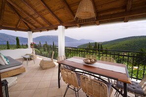 Un espace extérieur abrité, avec une table en bois et des chaises en osier, offrant une vue panoramique sur un paysage montagneux.