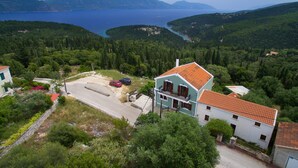 Zona residencial con una casa de dos pisos que tiene un balcón, rodeada de exuberante vegetación y vistas a un lago.