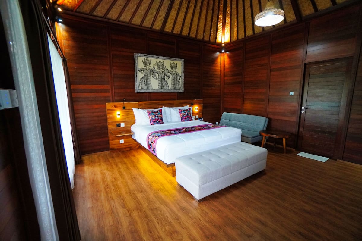 Une chambre avec un plafond en bois, un lit avec une literie blanche, un banc, une chaise et une porte en bois.